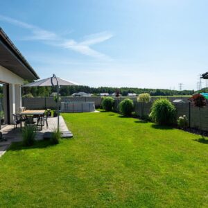 A beautiful garden with green grass, a patio table and umbrella visible, a house in beautiful summer weather, a very wide shot.